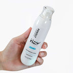 Hair removal and growth inhibitor spray held in a hand, featuring a sleek design and moisturizing formula.